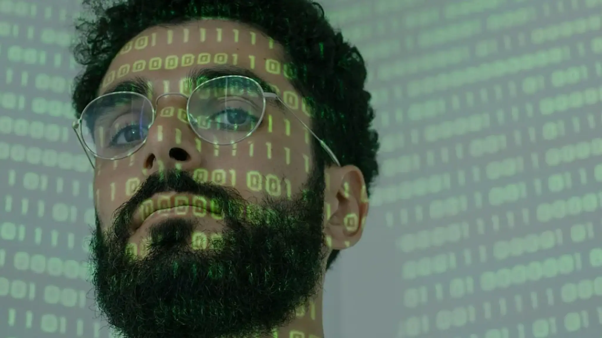 Portret van een man met bril en baard, waarop groene binaire code (nullen en enen) wordt geprojecteerd.