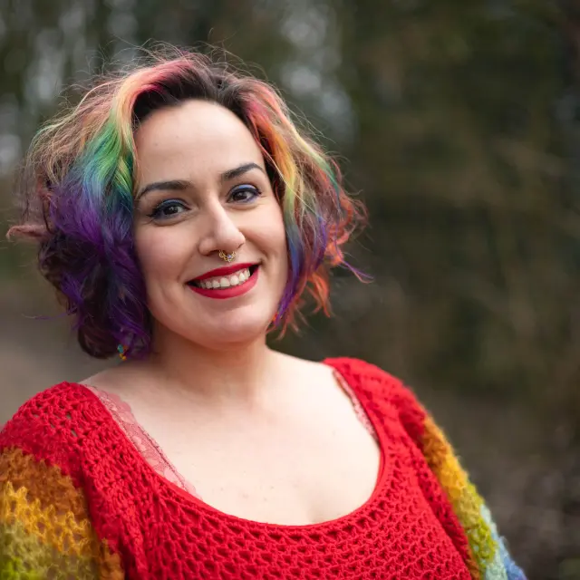 Jopie Louwe Kooijmans. Ze draagt een trui in verschillende kleuren en ook haar haar is in verschillende kleuren geverfd.