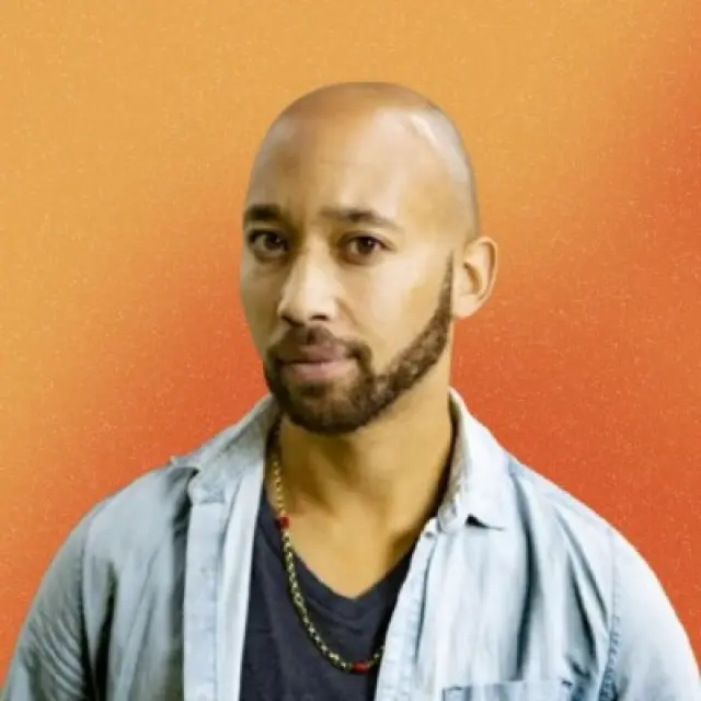 Osiris Hoepel kijkt een beetje schuin in de camera. Hij heeft een kaal hoofd, een korte baard, een donker T-shirt, een lichtblauw open overhemd en een ketting, tegen een oranje kleurverloop als achtergrond.