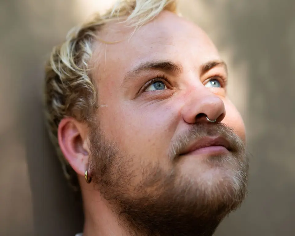 Close-up portret van Tijn de Jong, met kort blond haar, een baard, een neusring en een oorbel.