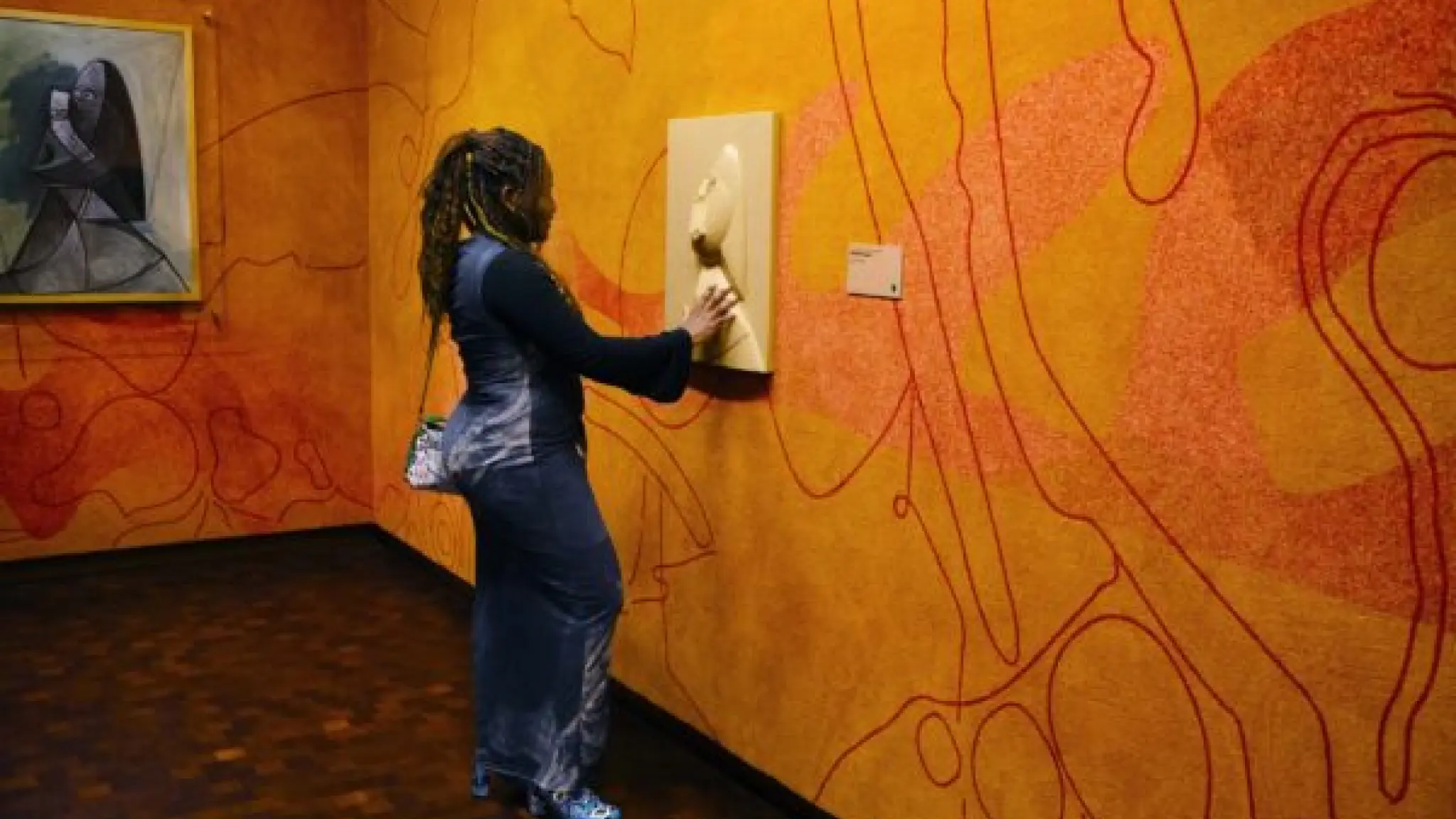 Een vrouw voelt aan een reliëfweergave van een schilderij. Het echte schilderij hangt links van haar aan de muur.