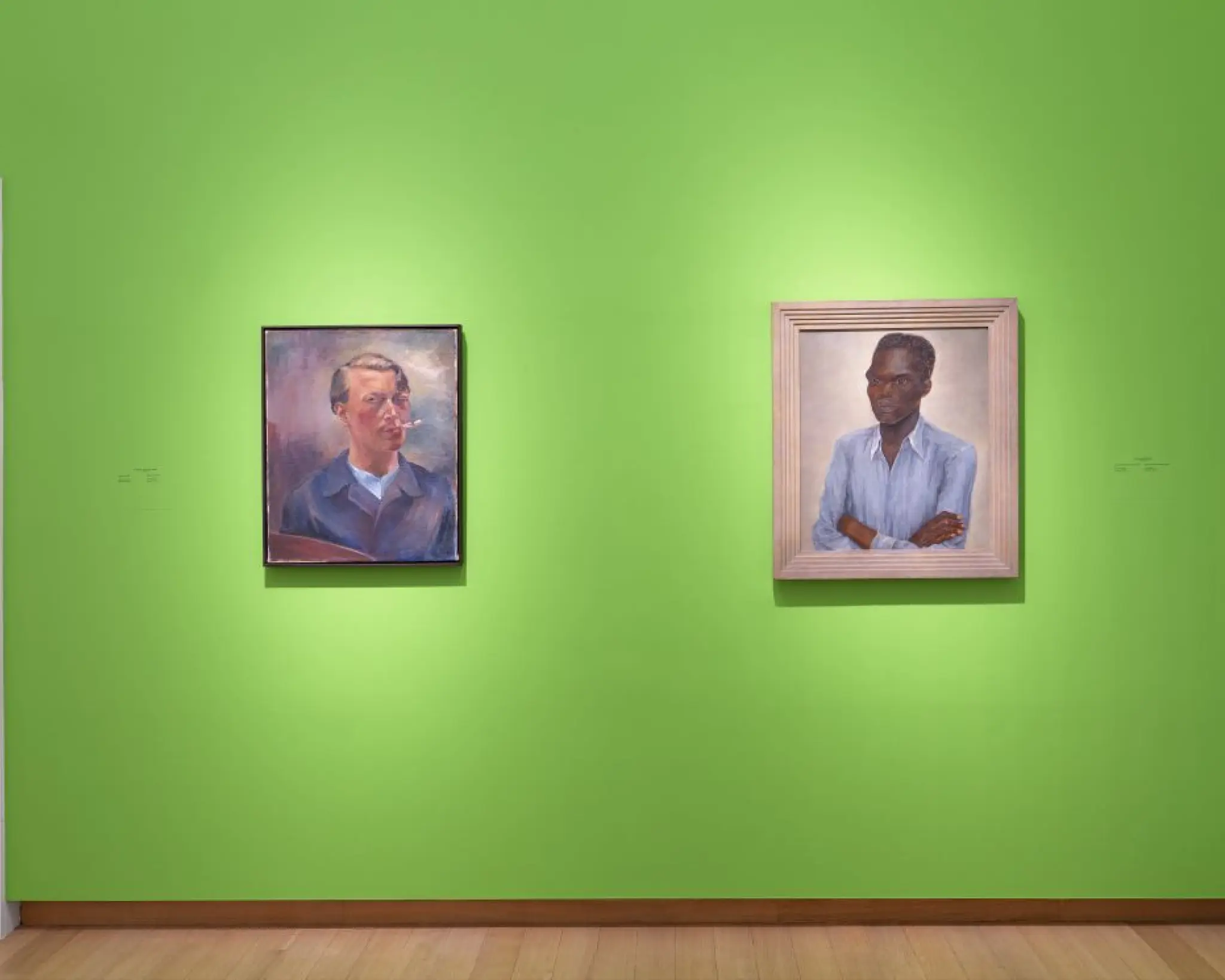 Twee portretschilderijen aan een felgroene museumwand: links een zelfportret van een man met pijp, rechts een portret van een man met donkere huid in een lichtblauw overhemd, armen over elkaar.