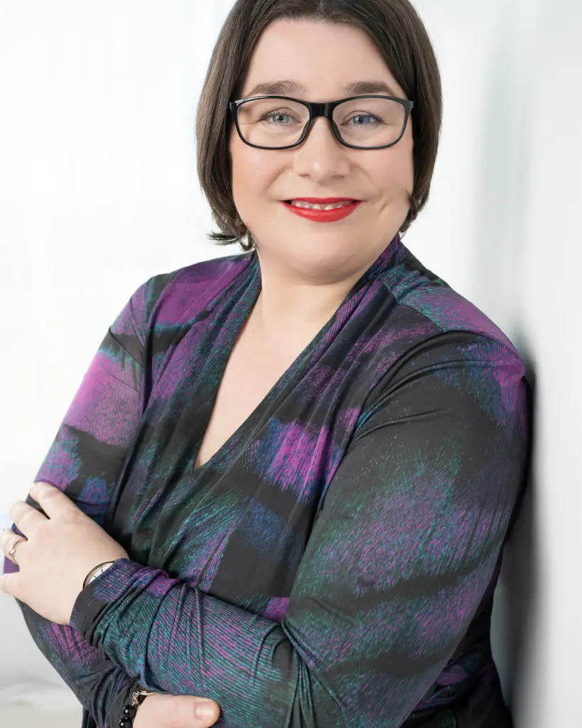 Marianne Dijkshoorn. Ze leunt tegen een witte muur en kijkt over haar linkerschouder naar de camera.