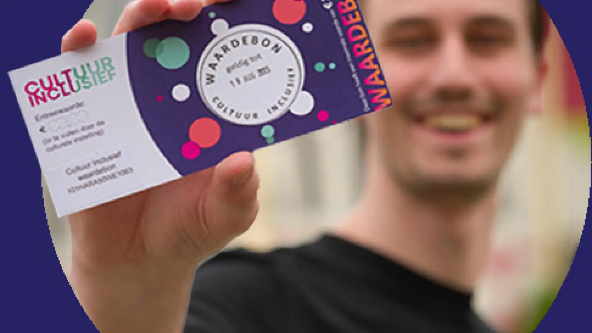 Een jonge man houdt lachend een cultuurwaardebon omhoog, waarbij de tekst en het kleurrijke ontwerp op de bon duidelijk zichtbaar zijn tegen een paarse achtergrond.