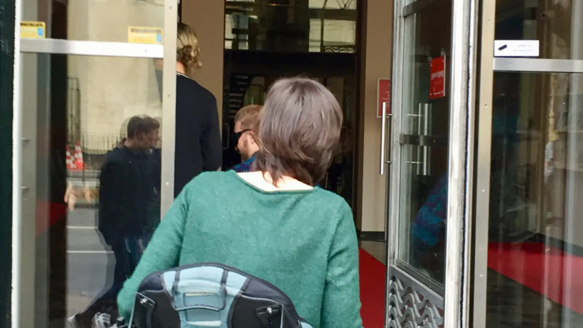 Een persoon in een rolstoel gaat door een openstaande deur naar binnen bij het Nationale Theater, Koninklijke Schouwburg.