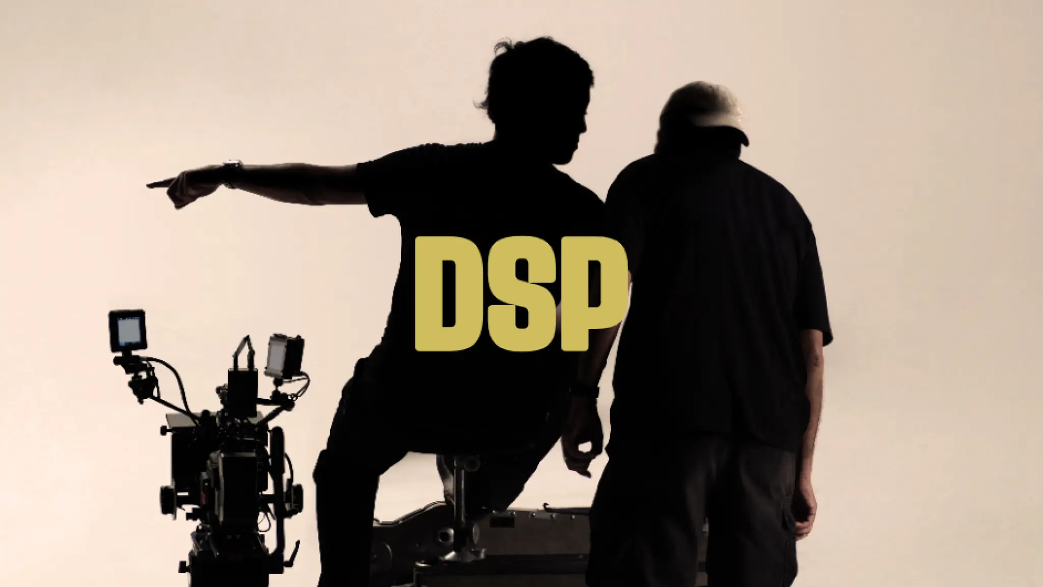 Silhouet van twee personen op een filmset. Eén persoon zit op een camera-opstelling en wijst naar links, terwijl de andere persoon ernaast staat. Op de voorgrond is professionele filmapparatuur zichtbaar. Midden in de afbeelding staat in grote gele letters de tekst “DSP”.