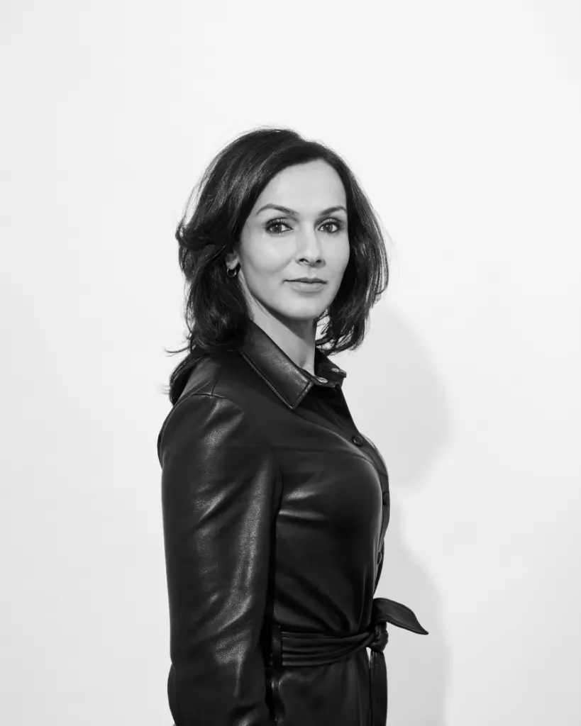 Zwart-wit portret van Jamila. Ze draagt een donkere leren jurk. Ze staat een kwartslag gedraaid en kijkt over haar rechterschouder naar de camera.