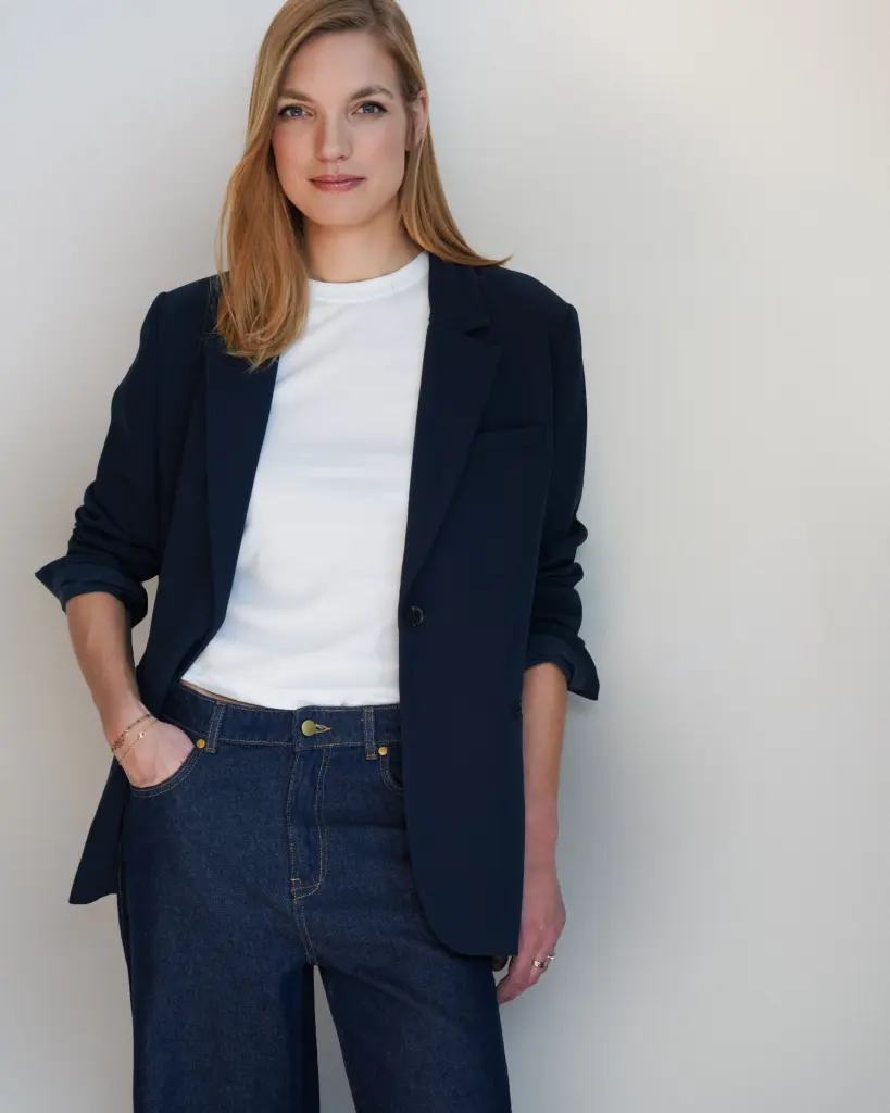 Julia Wolters kijkt met een neutrale blik recht in de camera. Ze draagt een spijkerbroek, wit t-shirt en donkerblauwe blazer. Haar blonde haren hangen los.