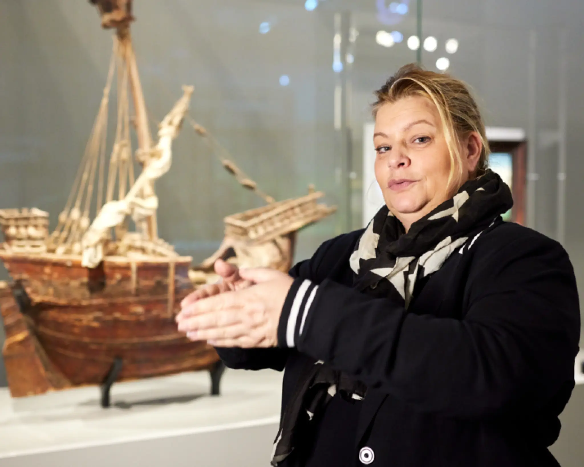 Een tolk Nederlandse Gebarentaal geeft uitleg bij een model van een schip.