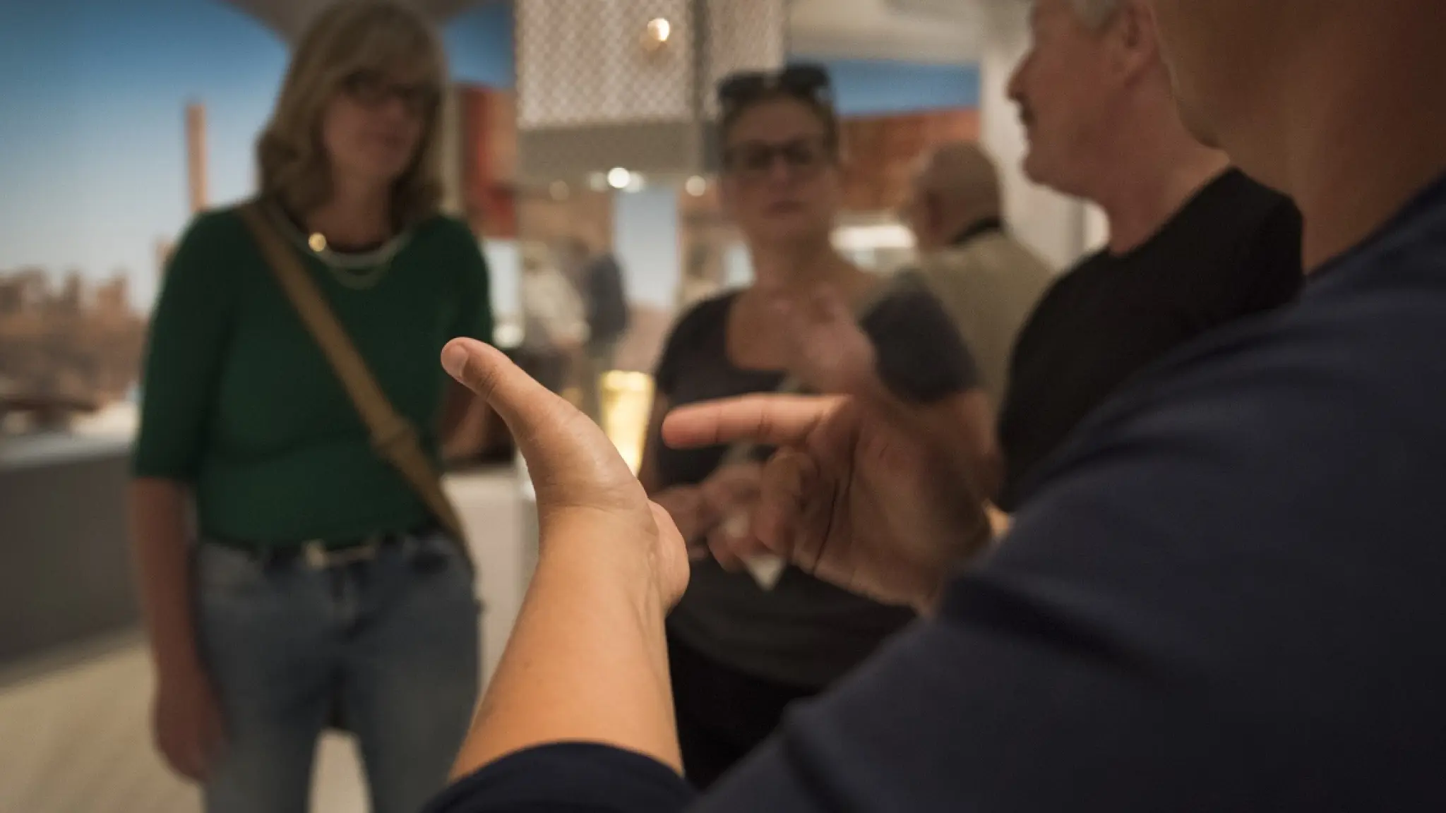 De handen van en tolk Nederlandse Gebarentaal vertaalt de rondleiding. Op de achtergrond zijn deelnemers aan de rondleiding te zien.