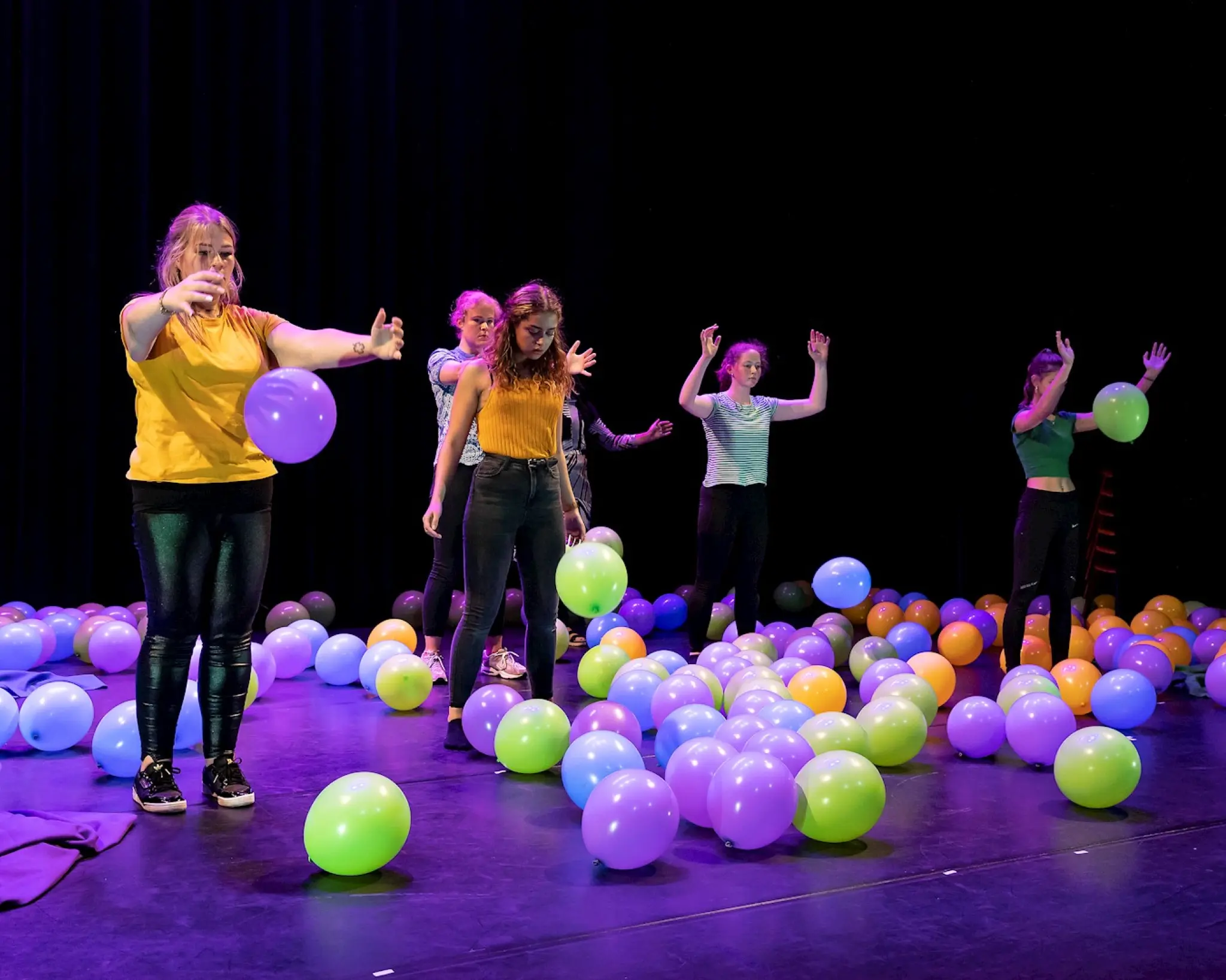 6 jonge mensen staan op het podium te midden van een zee aan ballonnen.