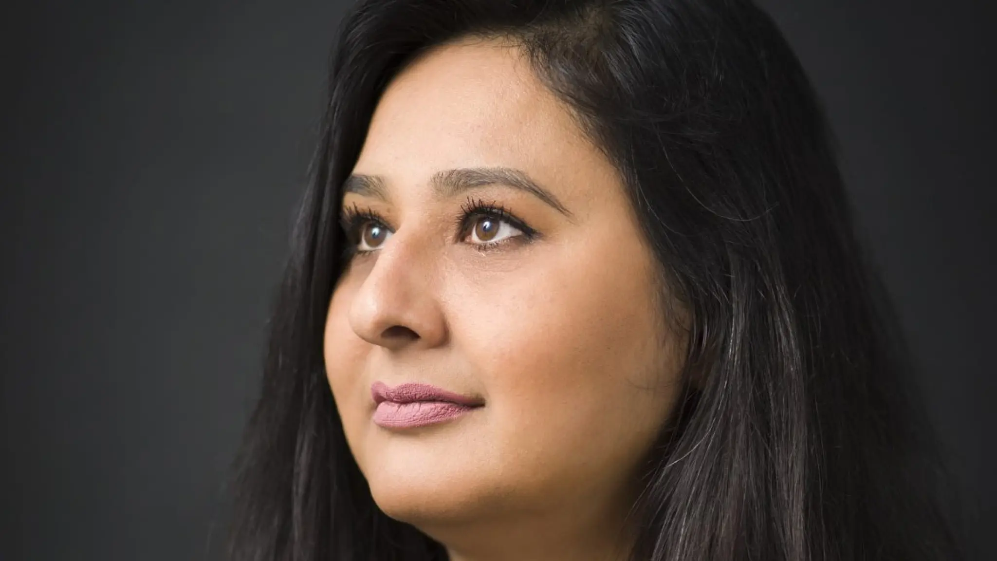 Portret van Sahar Noor: een vrouw met lang, donker haar die naar links kijkt, met een neutrale uitdrukking op haar gezicht tegen een donkere achtergrond.