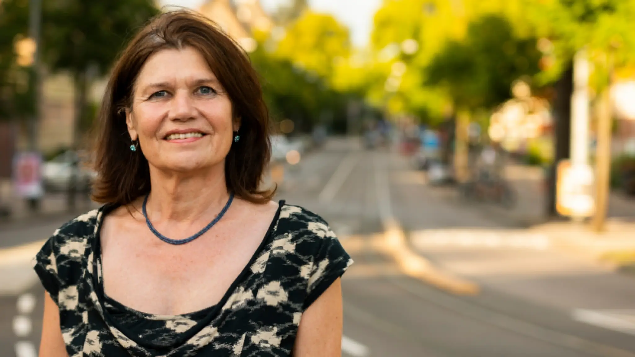De glimlachende Anja Hiddinga staat op een straat met tramrails en bomen op de achtergrond.